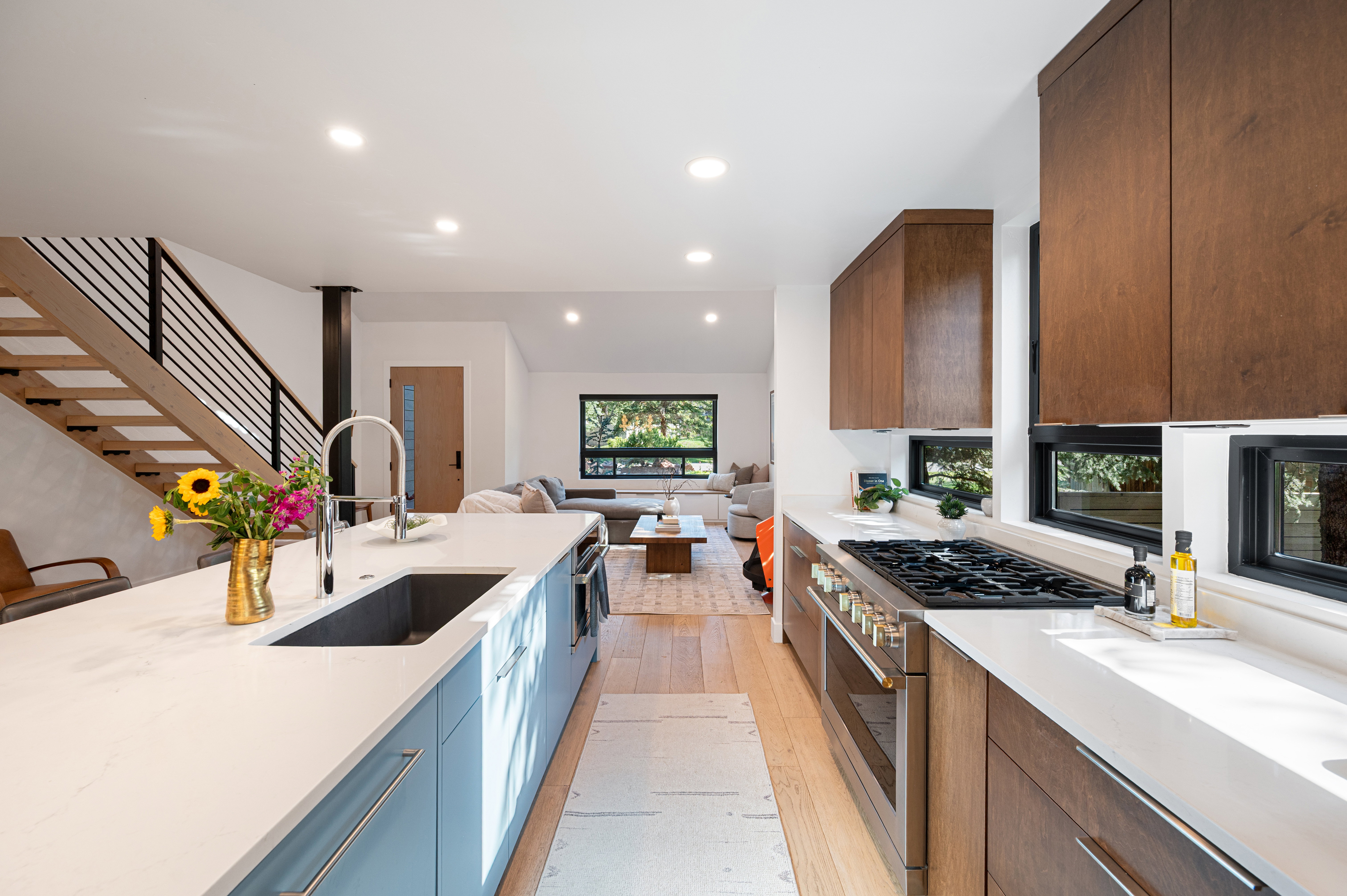 Modern kitchen featuring a spacious island with an integrated sink, light-toned countertops, wood-finish cabinetry, and stainless steel appliances, including a gas range