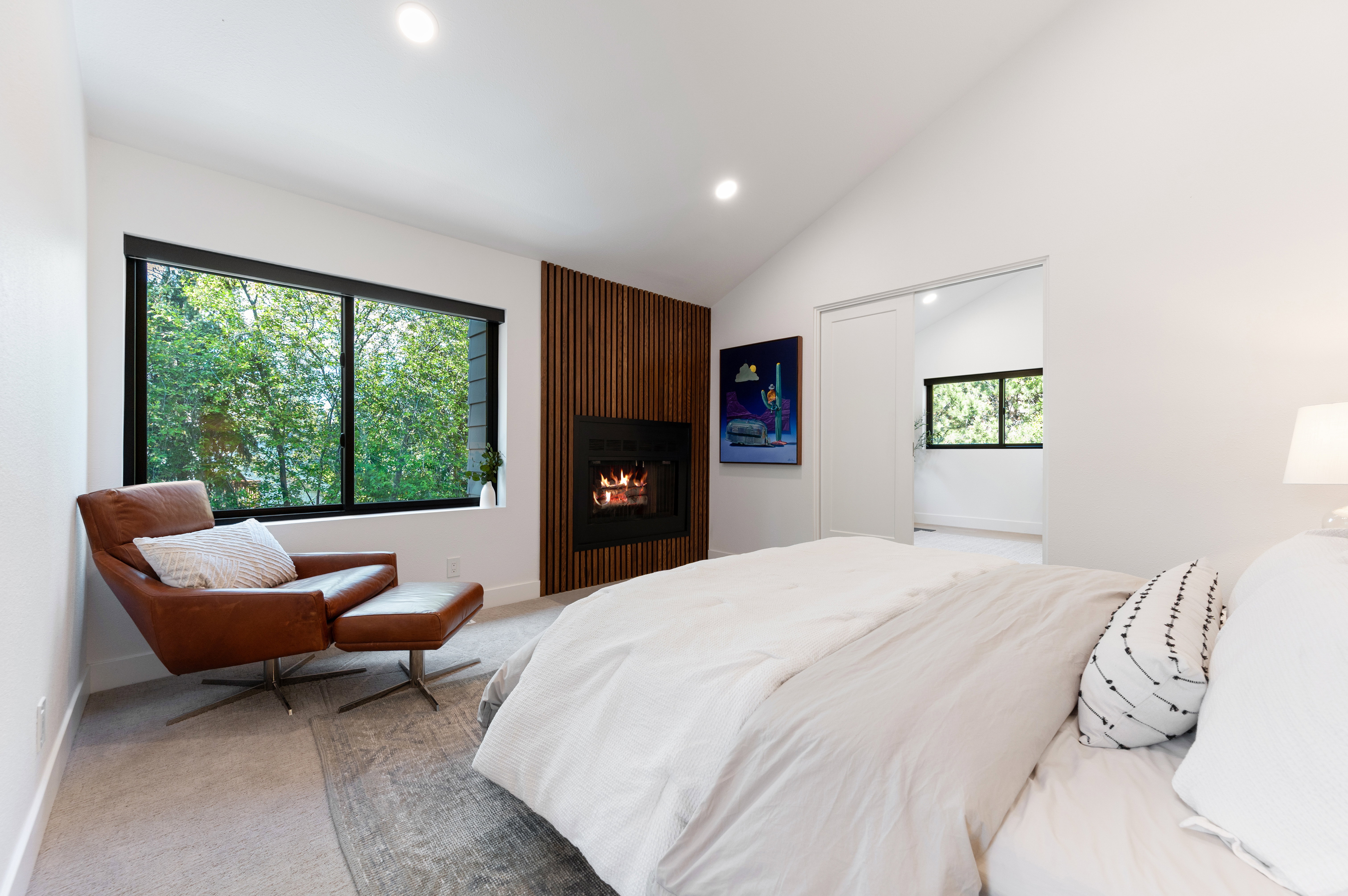 Vaulted ceilings enhance this room featuring a fireplace with a slatted wood surround, a large window, recessed lighting, and soft carpeting