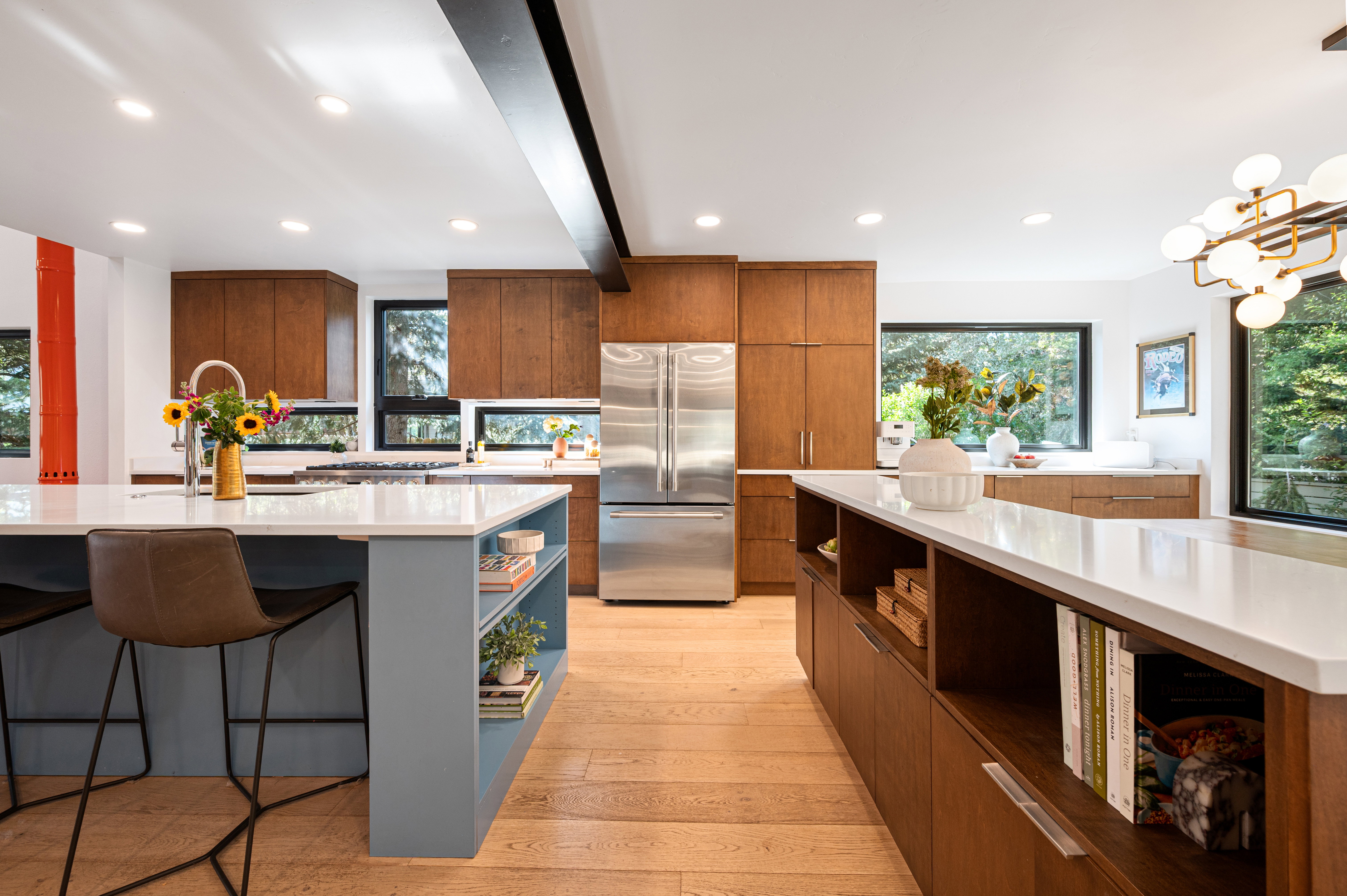 Expansive kitchen featuring a large central island with seating, additional island with built-in shelving, wood-finish cabinetry, stainless steel refrigerator, and recessed lighting