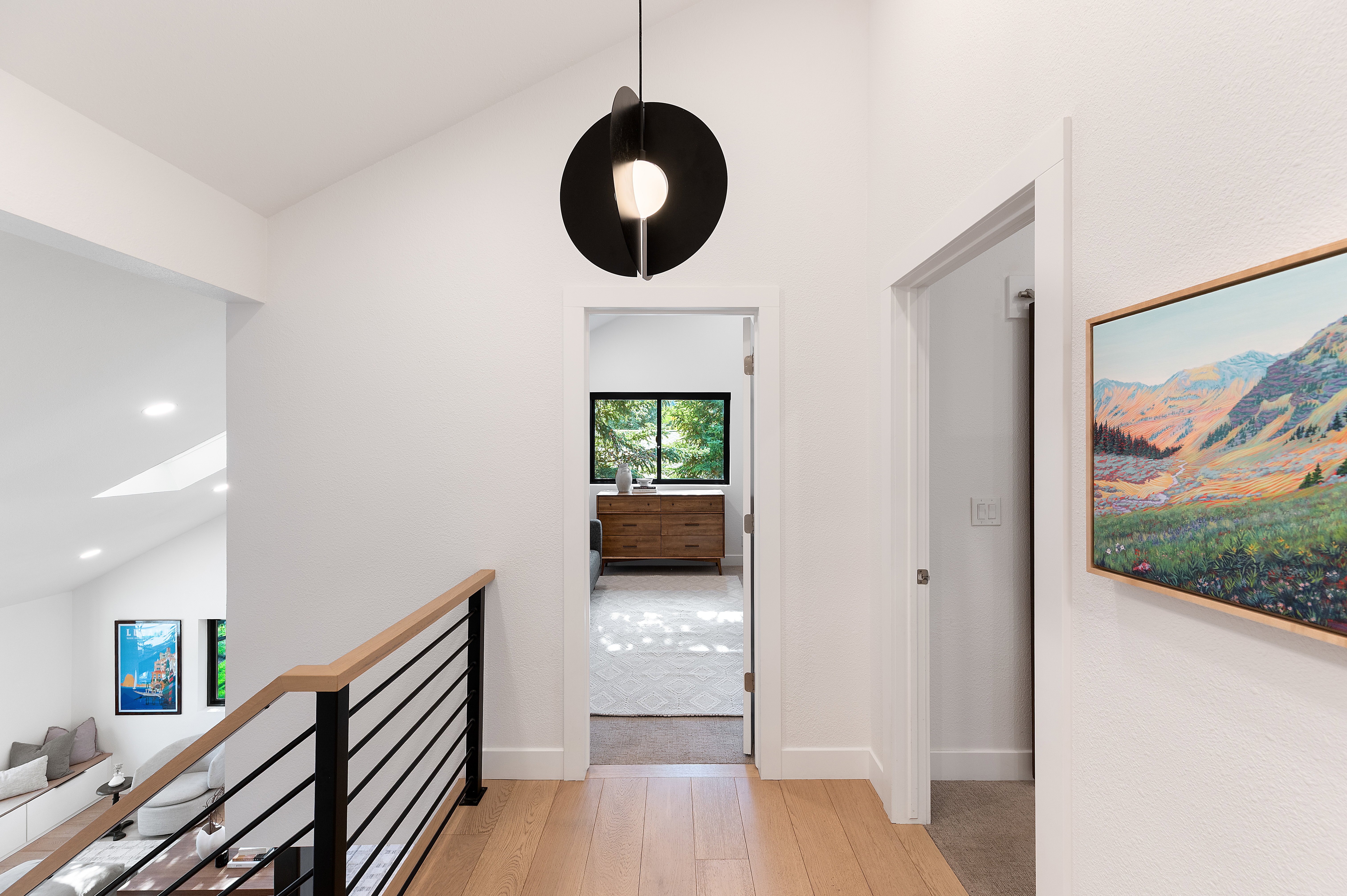 Vaulted hallway featuring a modern black pendant light, light wood-finish flooring, and a contemporary black metal and wood railing