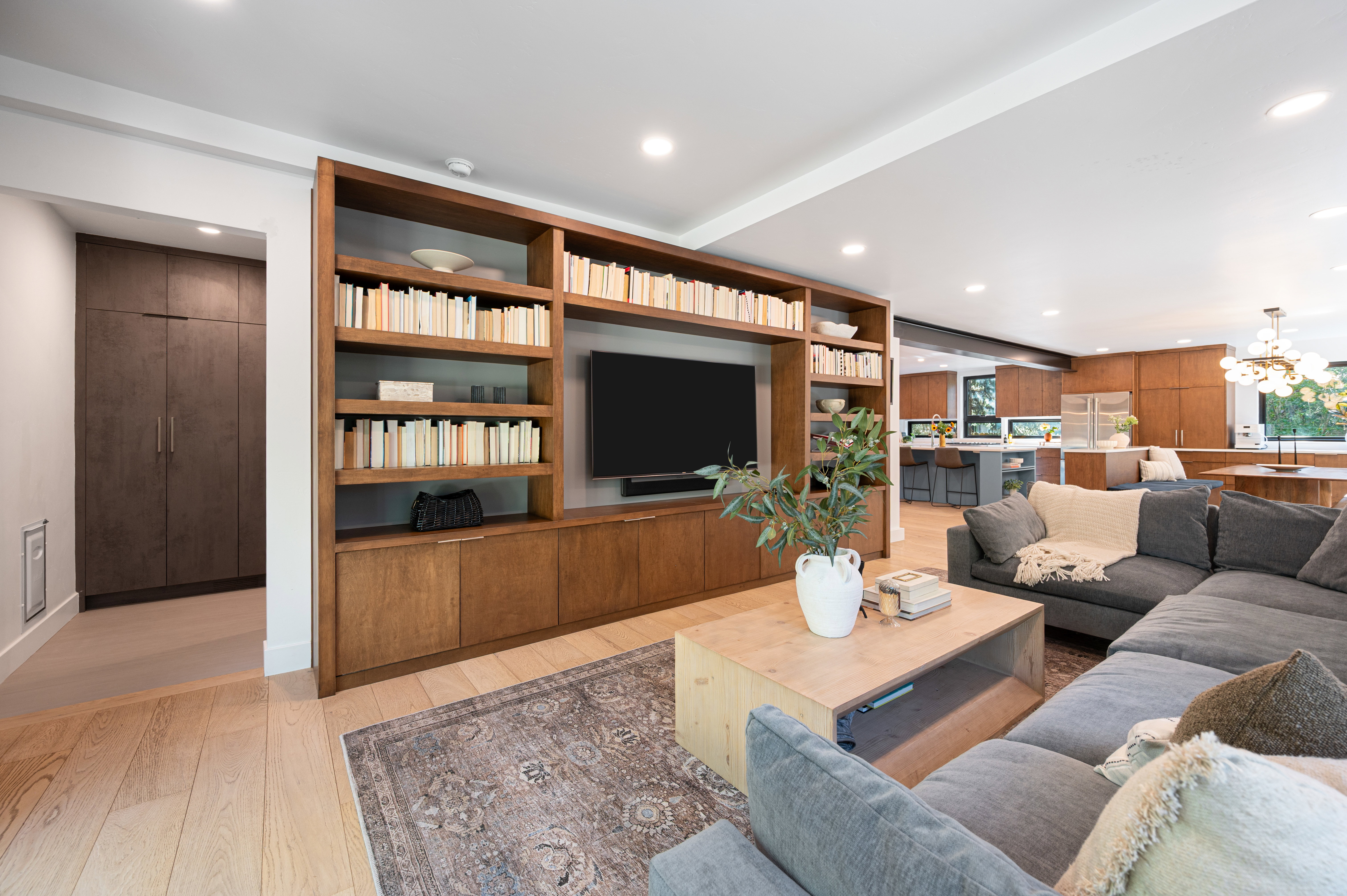 Living area featuring light wood-finish flooring, recessed lighting, and a built-in entertainment center with open shelving and closed cabinetry