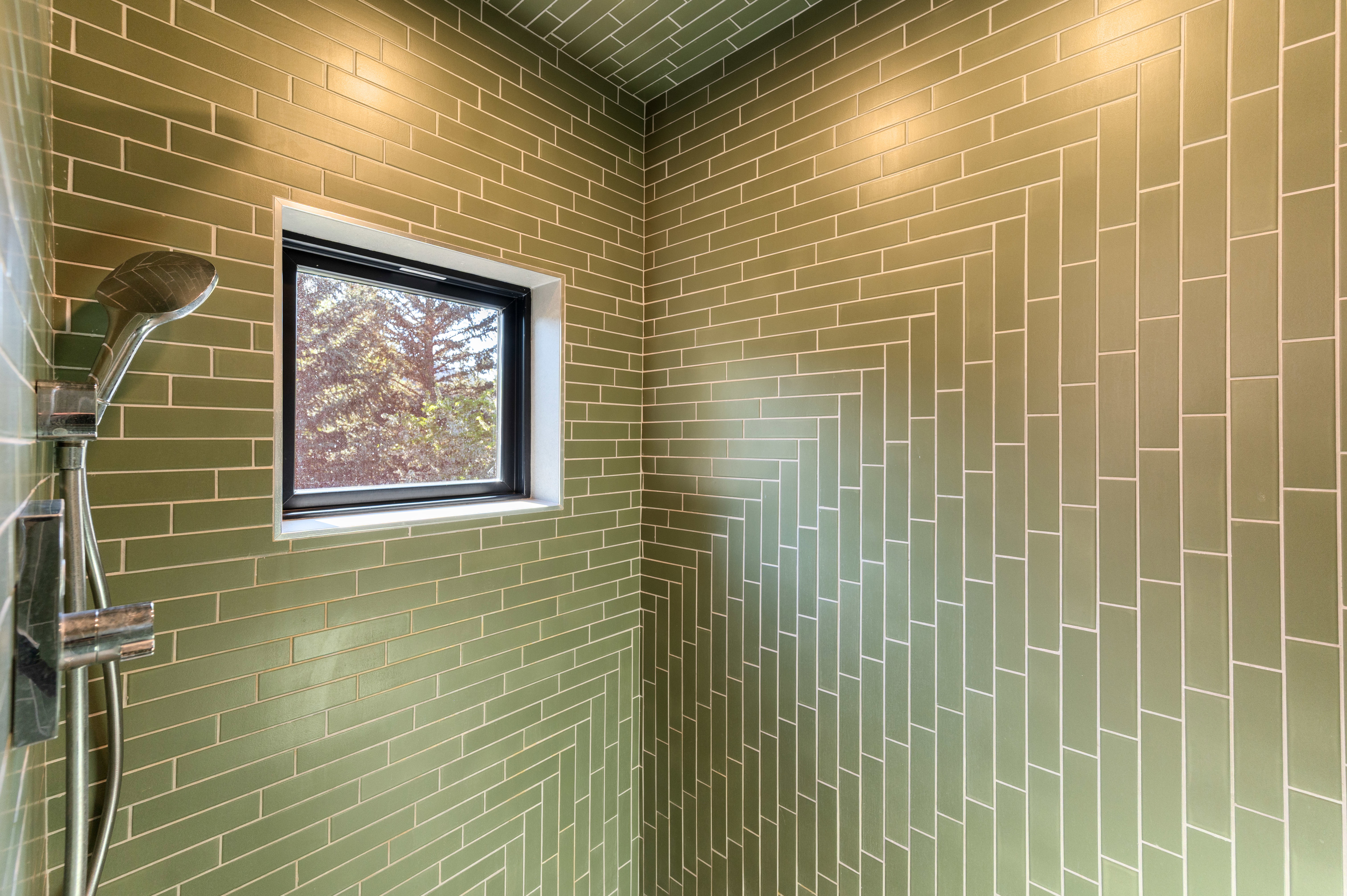 Shower enclosure featuring green subway tile, a black-framed window, and a wall-mounted shower fixture