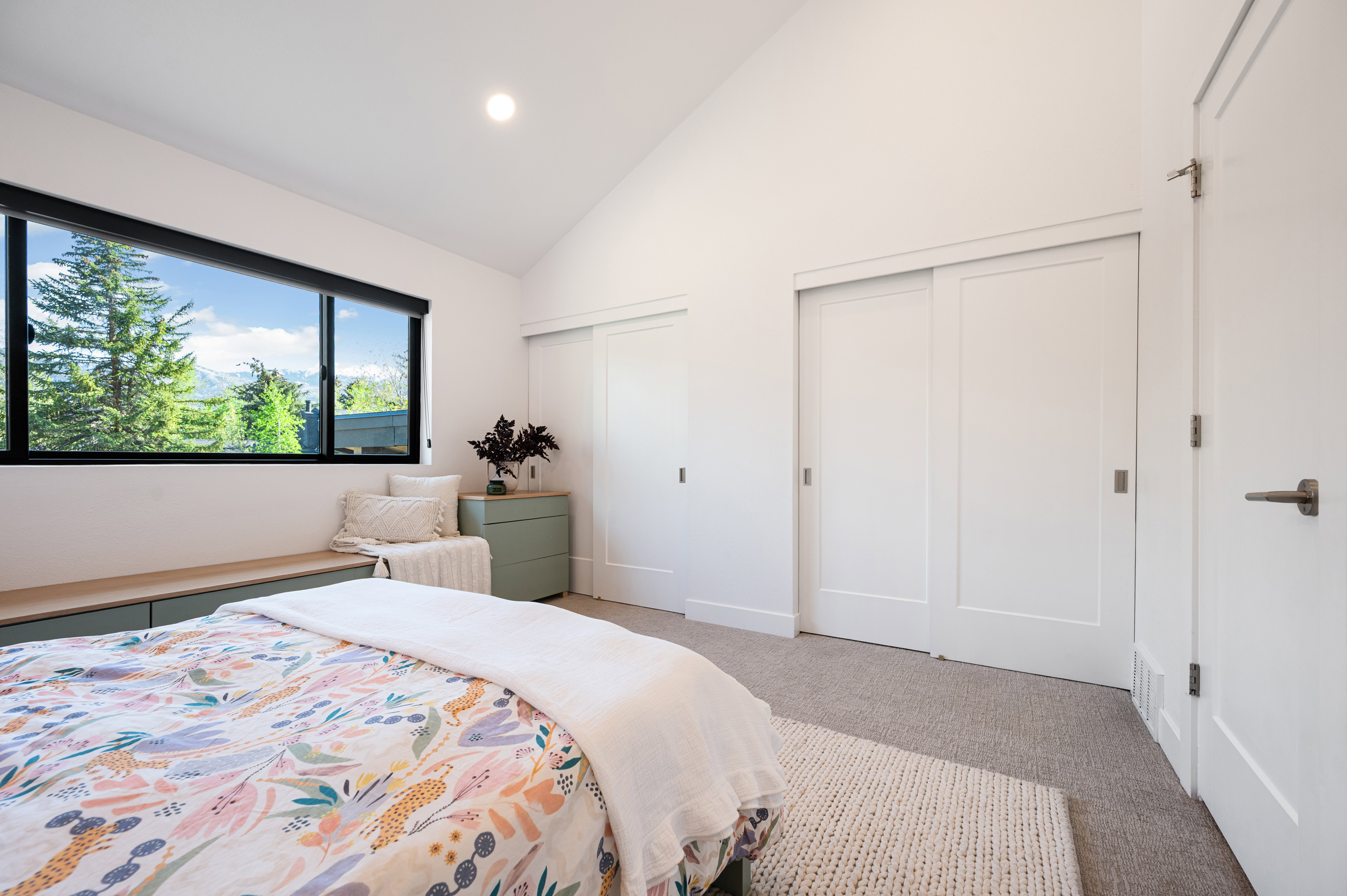 Vaulted white ceilings featuring recessed lighting, a panoramic window with exterior scenery, a built-in window bench, two sliding closet doors, and light gray carpeting