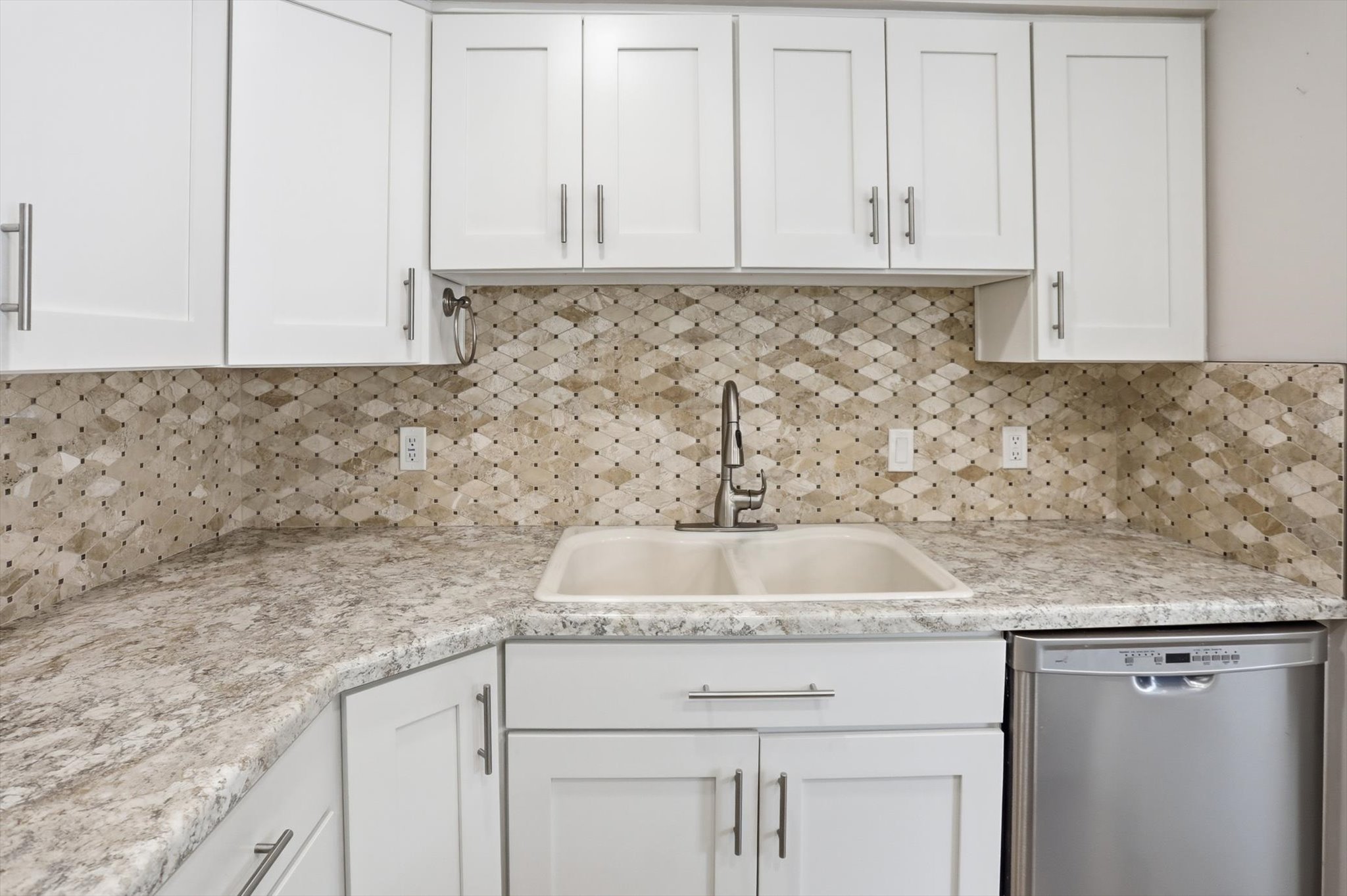 Kitchen featuring white shaker-style cabinetry, a patterned tile backsplash, light-toned countertops, and a dual-basin sink with a pull-down faucet
