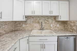 Kitchen featuring white shaker-style cabinetry, a patterned tile backsplash, light-toned countertops, and a dual-basin sink with a pull-down faucet