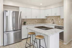 Contemporary kitchen featuring an island with a built-in cooktop, white shaker cabinetry, stainless steel appliances, mosaic tile backsplash, and light-toned countertops
