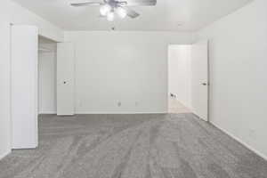 Spacious room featuring light gray carpeting, neutral white walls, and a ceiling fan with integrated lighting