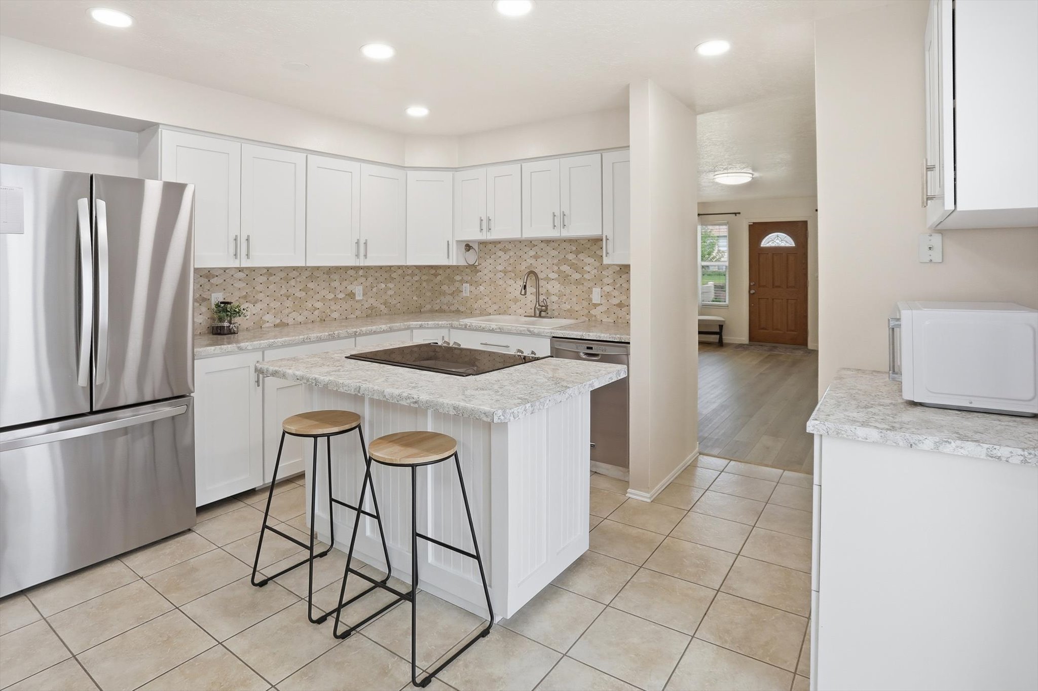 Modern kitchen featuring white cabinetry, light-colored countertops, a tile backsplash, stainless steel appliances, and a central island with an integrated cooktop