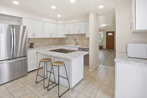 Modern kitchen featuring white cabinetry, light-colored countertops, a tile backsplash, stainless steel appliances, and a central island with an integrated cooktop