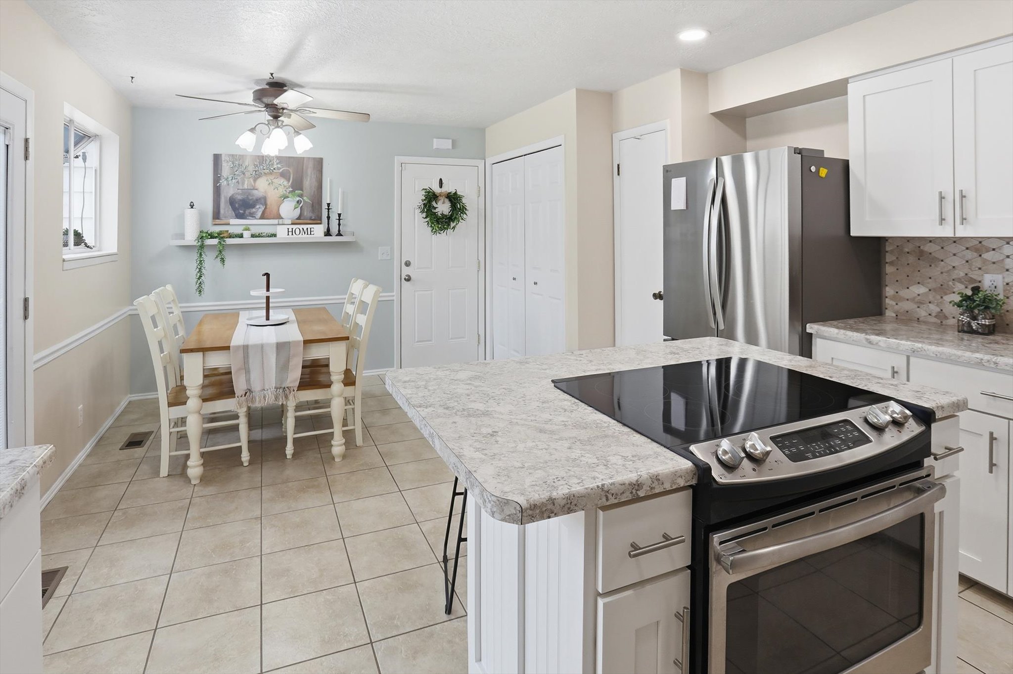 Integrated kitchen and dining area featuring a built-in cooktop, stainless steel refrigerator, white cabinetry, light-toned countertops, and neutral tile flooring