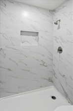 Shower featuring large format white tiled walls with gray veining, a built-in shower niche, and a brushed nickel shower head and control