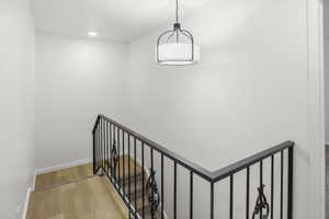 Staircase with wood-finish landing, wrought iron railing with decorative scrollwork, and a modern drum pendant light