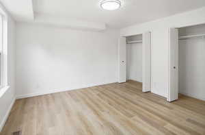 Spacious room featuring light wood-finish flooring, bright white walls, and a modern flush-mount ceiling light
