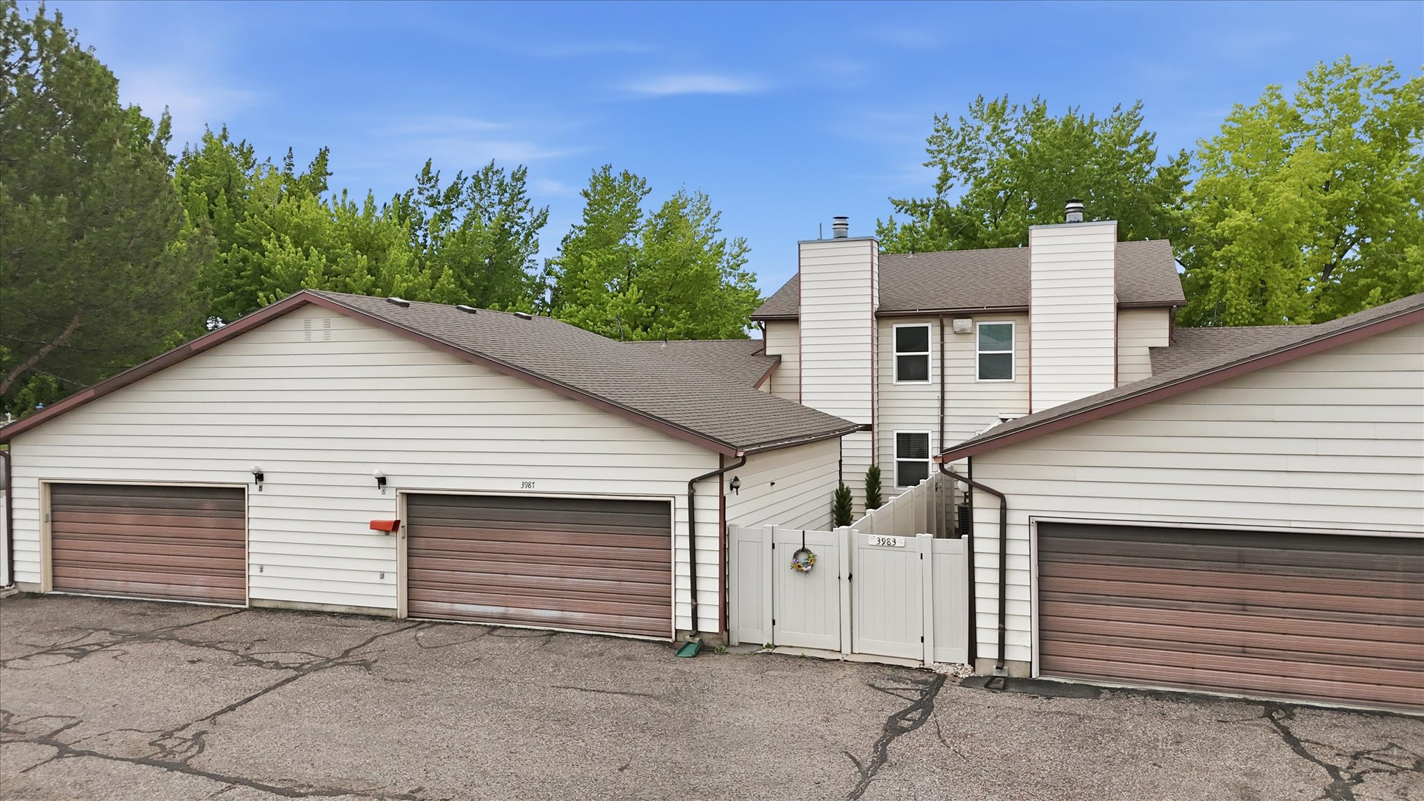 Exterior featuring white siding, brown wood-finish garage doors, and a white privacy fence