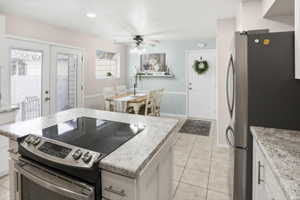 Kitchen featuring an island with built-in range, light-toned tiled flooring, white cabinetry, and granite-look countertops