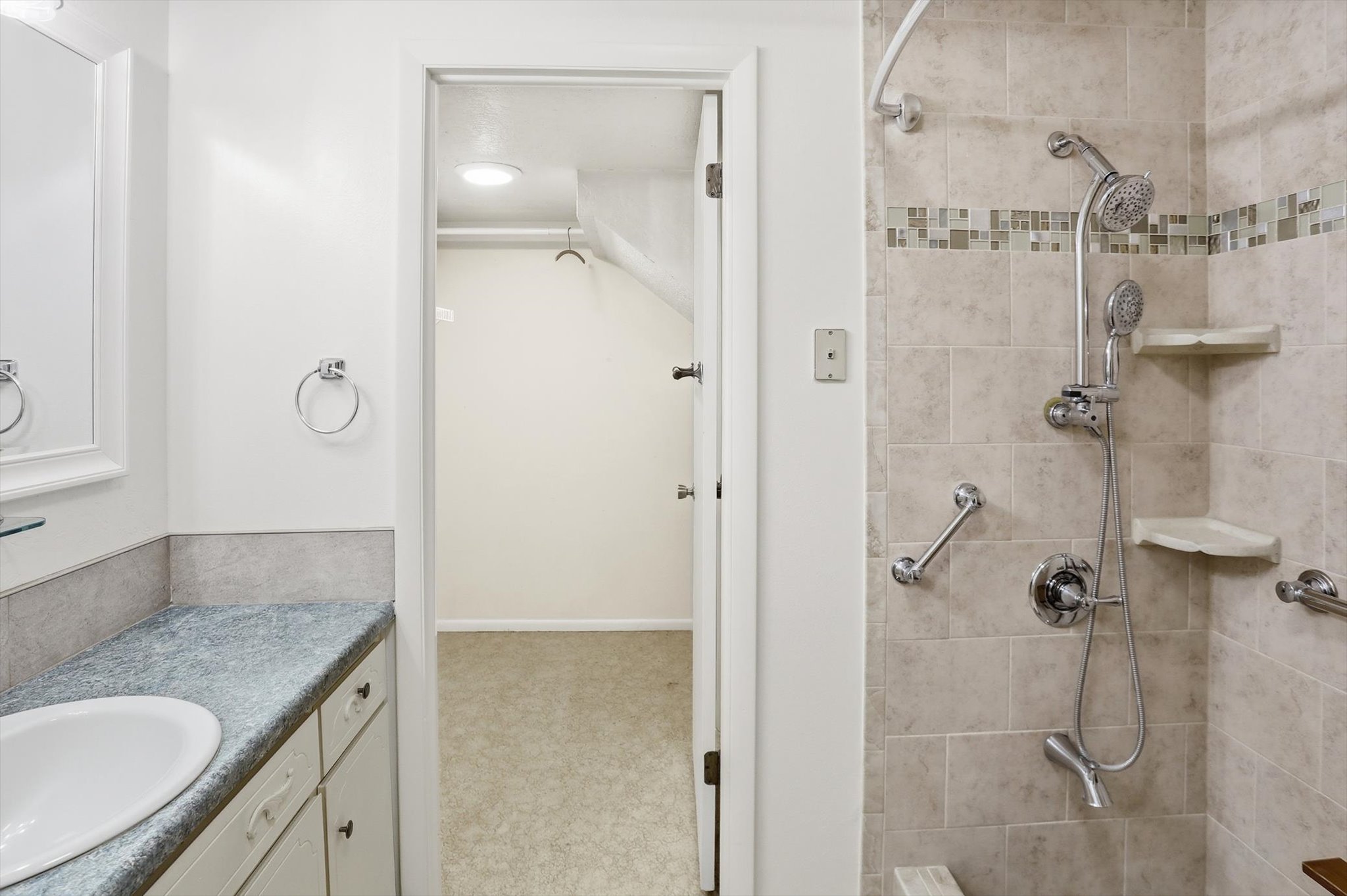 Bathroom featuring a tiled shower with mosaic accent band, multiple shower heads, and built-in shelving