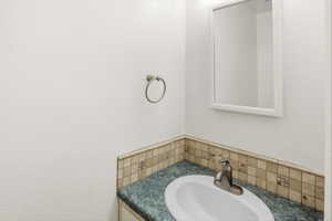 Vanity featuring an oval undermount sink with a brushed nickel faucet, a green speckled countertop, and a mosaic tile backsplash