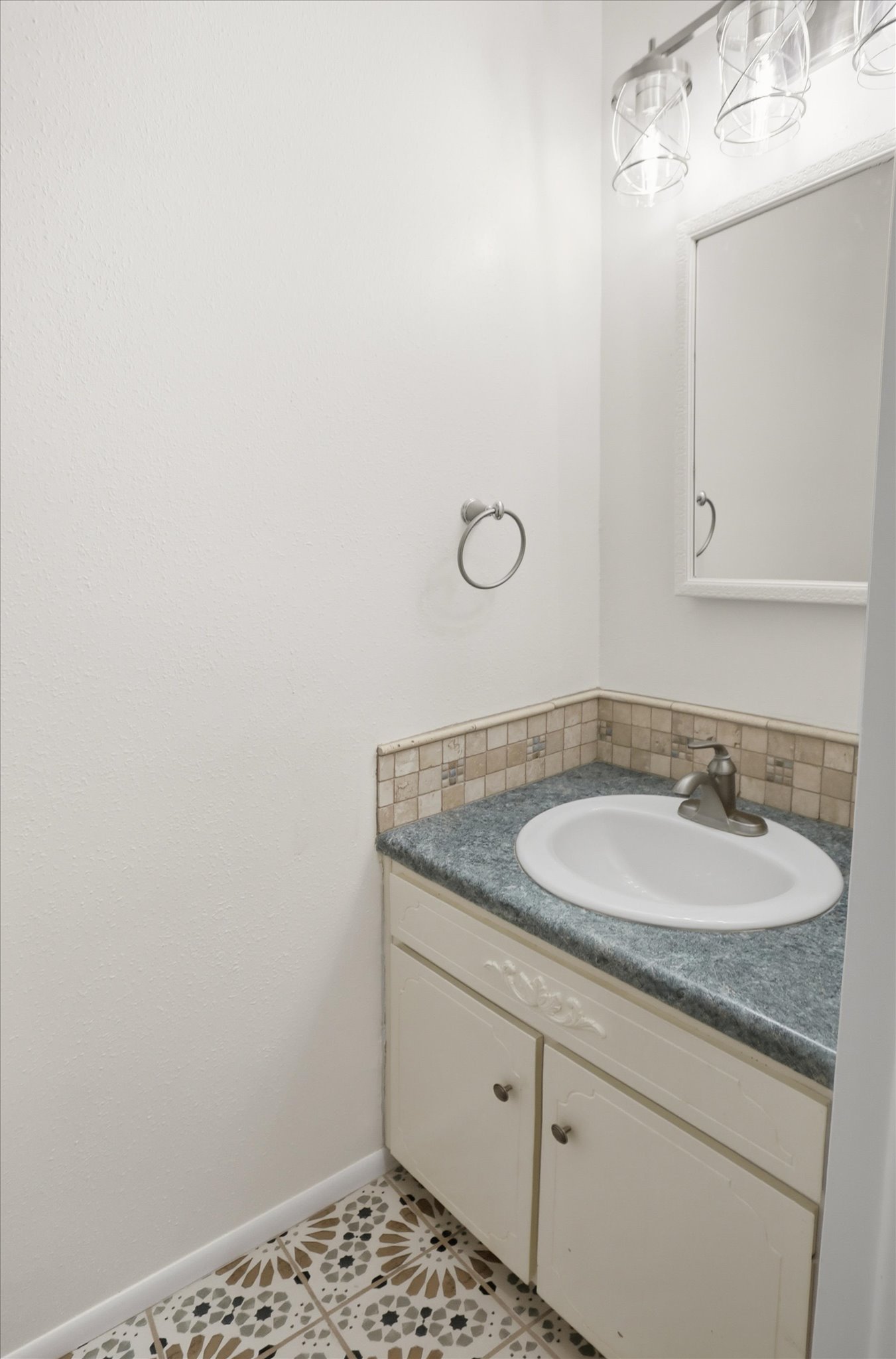 Bathroom vanity featuring a drop-in sink, gray countertop, mosaic tile backsplash, and decorative flooring