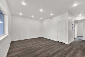 Spacious room featuring wood-finish flooring, recessed lighting, white trim, a solid panel interior door, and a large window