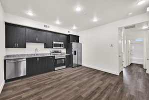 Kitchen featuring dark wood-finish cabinetry with stainless steel hardware, light speckled countertops, a white subway tile backsplash, and stainless steel appliances