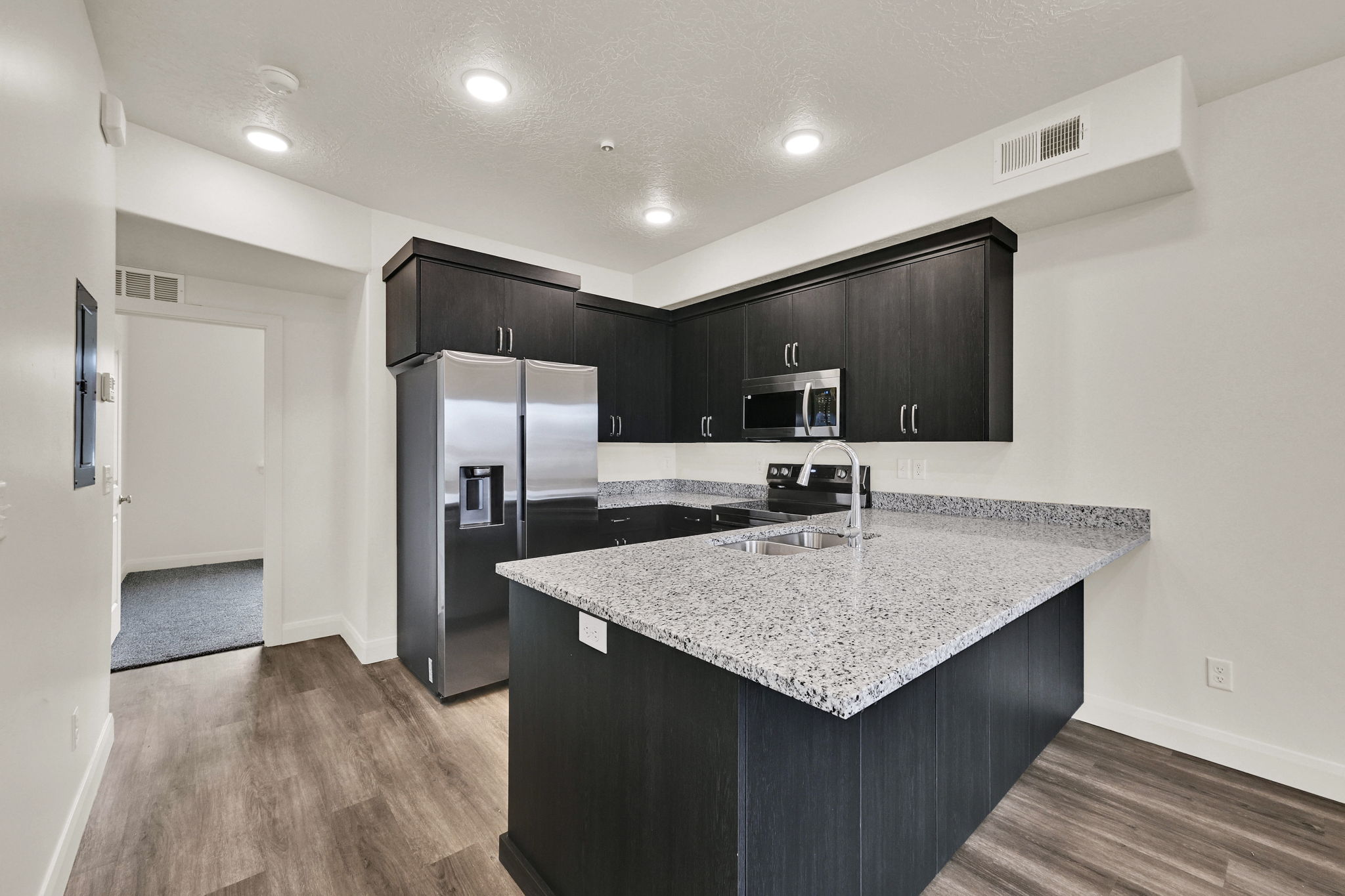 Kitchen featuring dark wood-finish cabinetry, light speckled countertops, stainless steel appliances, and wood-finish flooring