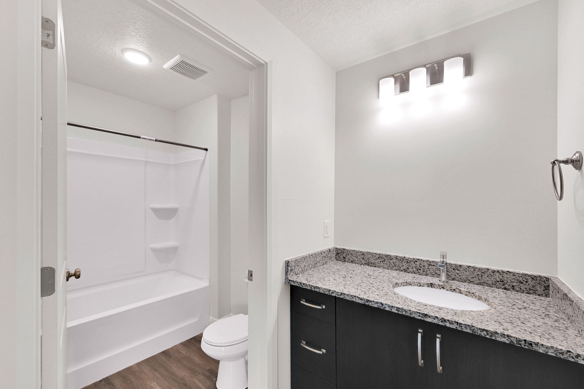 Modern bathroom featuring a dark wood-finish vanity with a light speckled countertop, under-mount sink, and chrome faucet