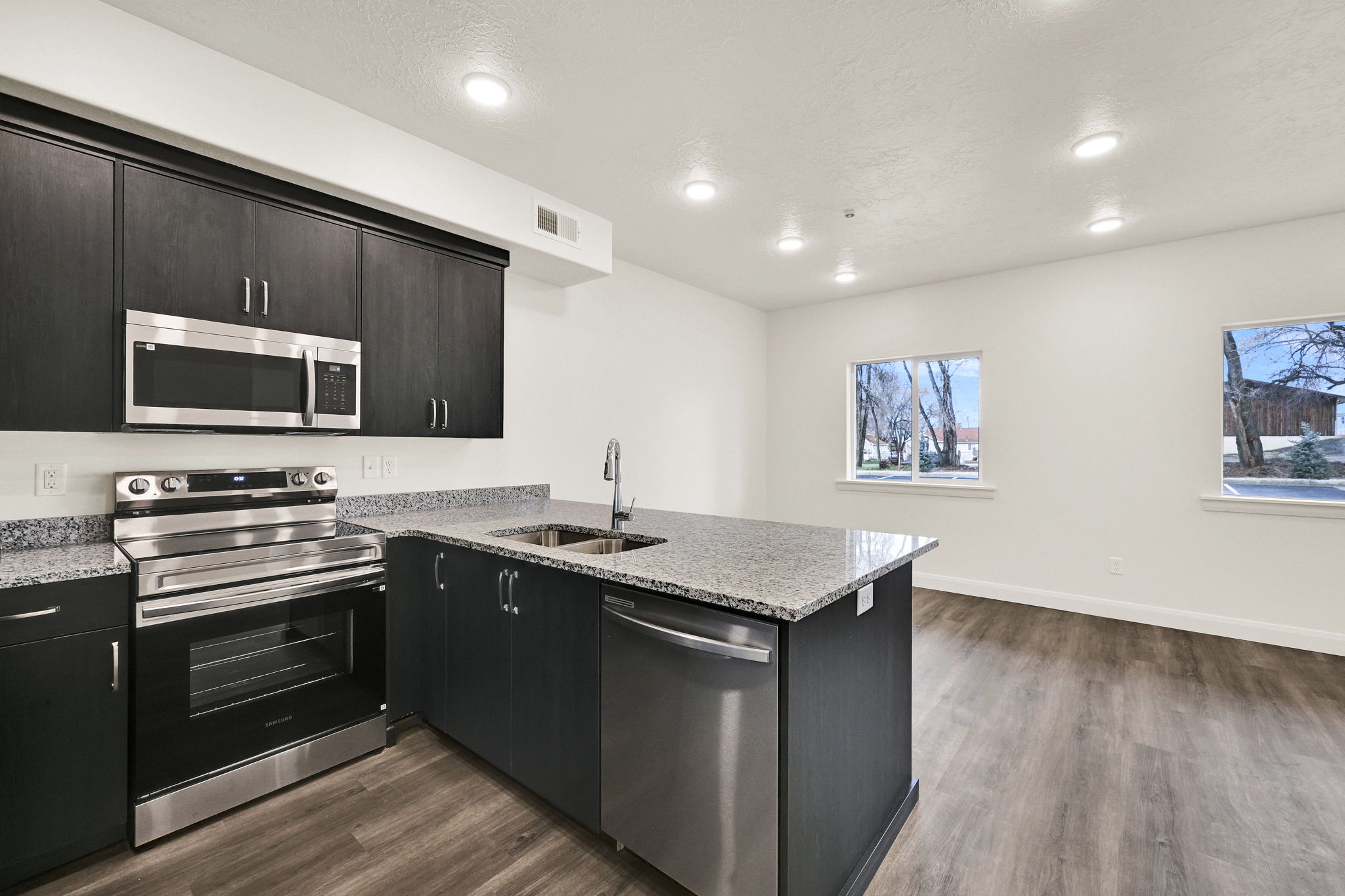 Kitchen island featuring a stainless steel sink and dishwasher, complemented by dark wood-finish cabinetry, granite countertops, and wood-finish flooring