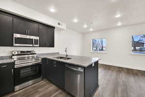 Kitchen island featuring a stainless steel sink and dishwasher, complemented by dark wood-finish cabinetry, granite countertops, and wood-finish flooring