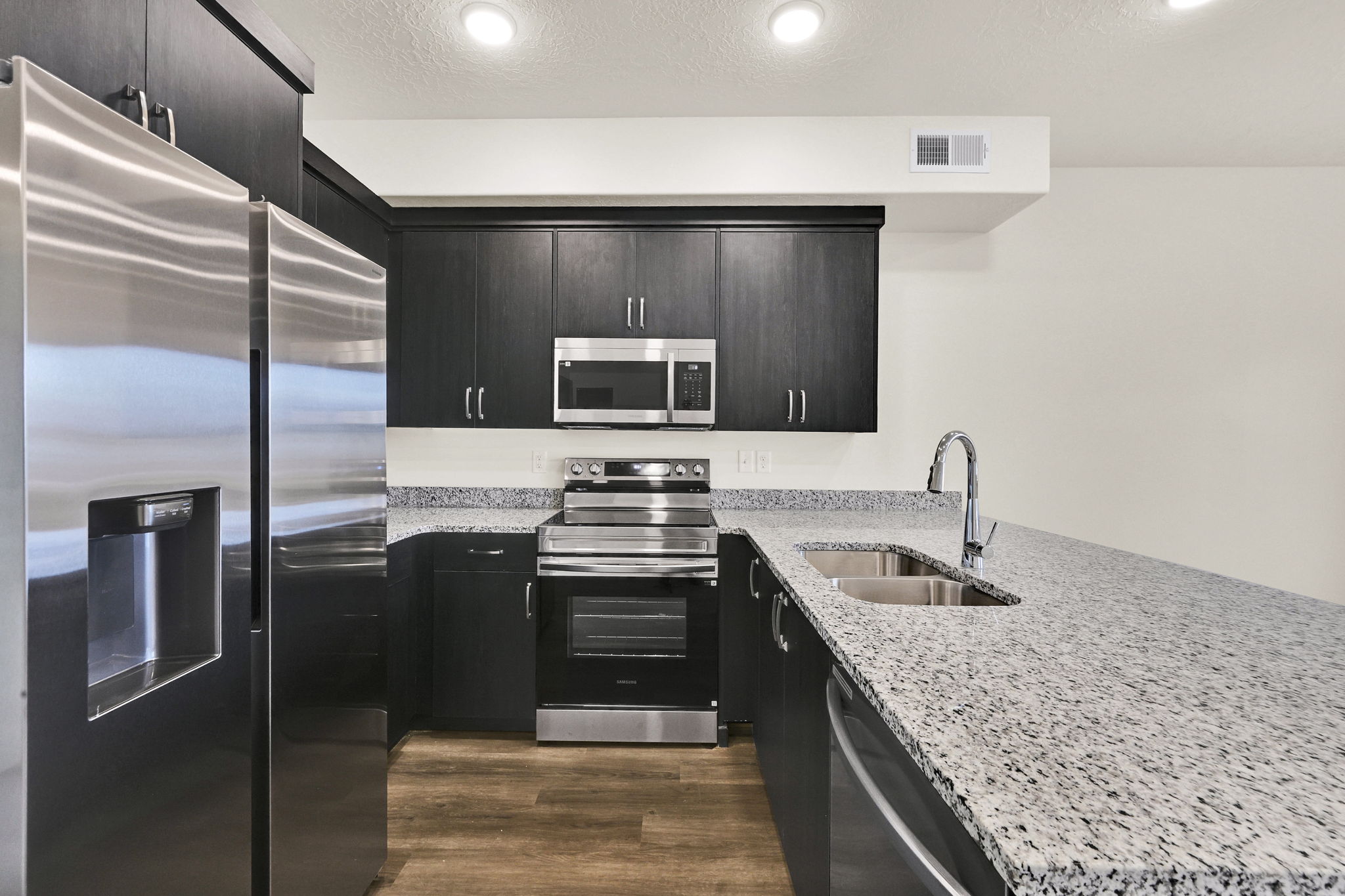 Kitchen featuring dark wood-finish cabinetry, stainless steel appliances, speckled stone countertops, and wood-finish flooring