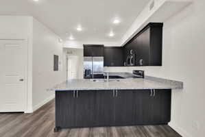 Modern kitchen featuring dark wood-finish cabinetry, light speckled countertops, and stainless steel appliances including a refrigerator, microwave, and range