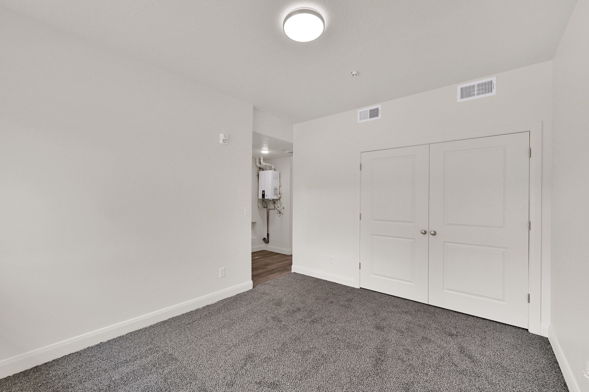 Wall-to-wall carpeting in a neutral tone, white baseboards, and a pair of white doors with silver knobs