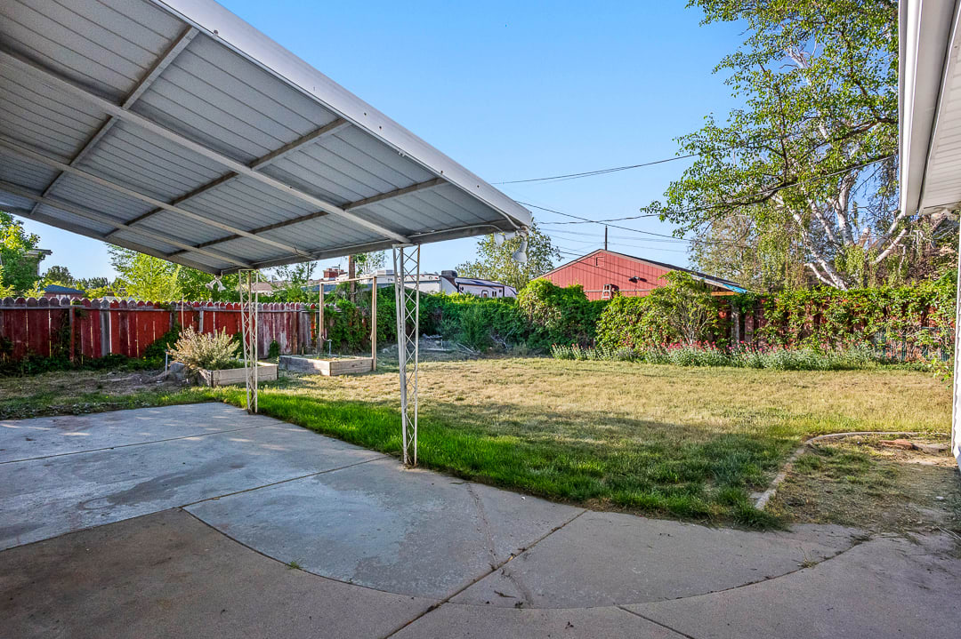 Expansive backyard featuring a concrete patio, covered carport structure, and perimeter fencing