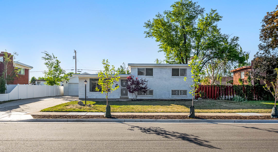 White painted brick exterior featuring a two-car garage, concrete driveway, and a fenced backyard