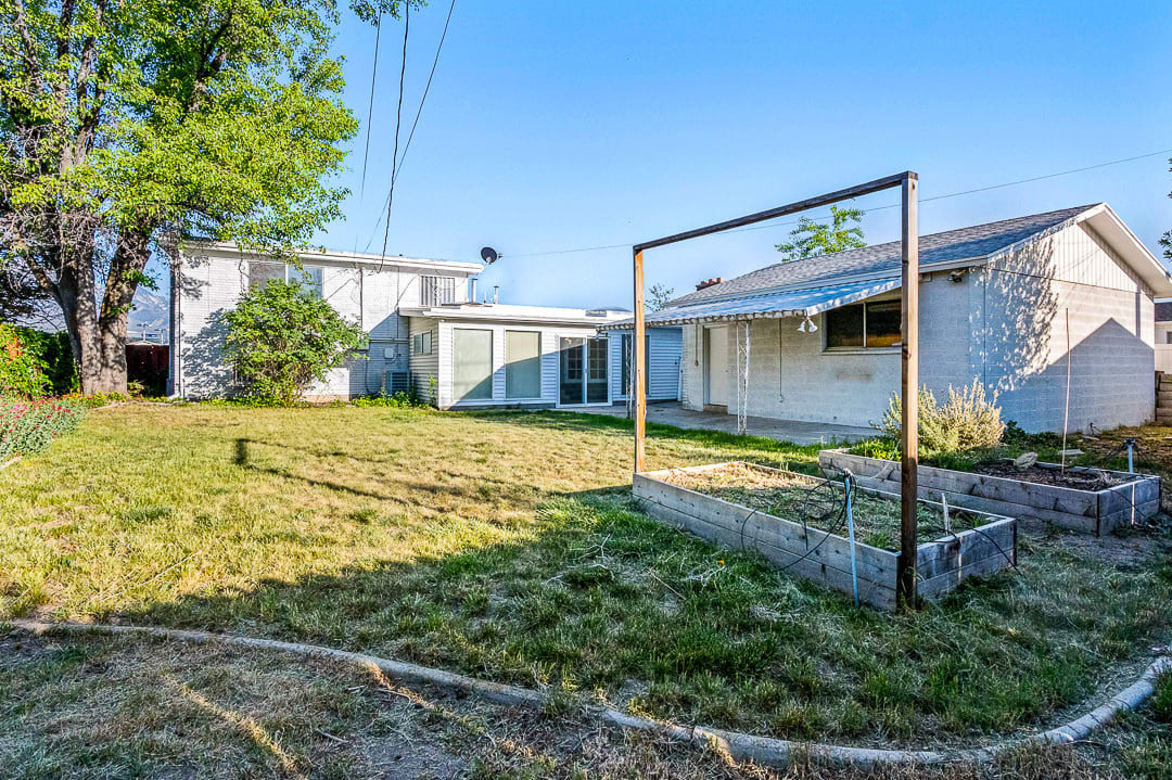 Expansive backyard featuring two raised garden beds, a mature tree, and a detached structure with an awning