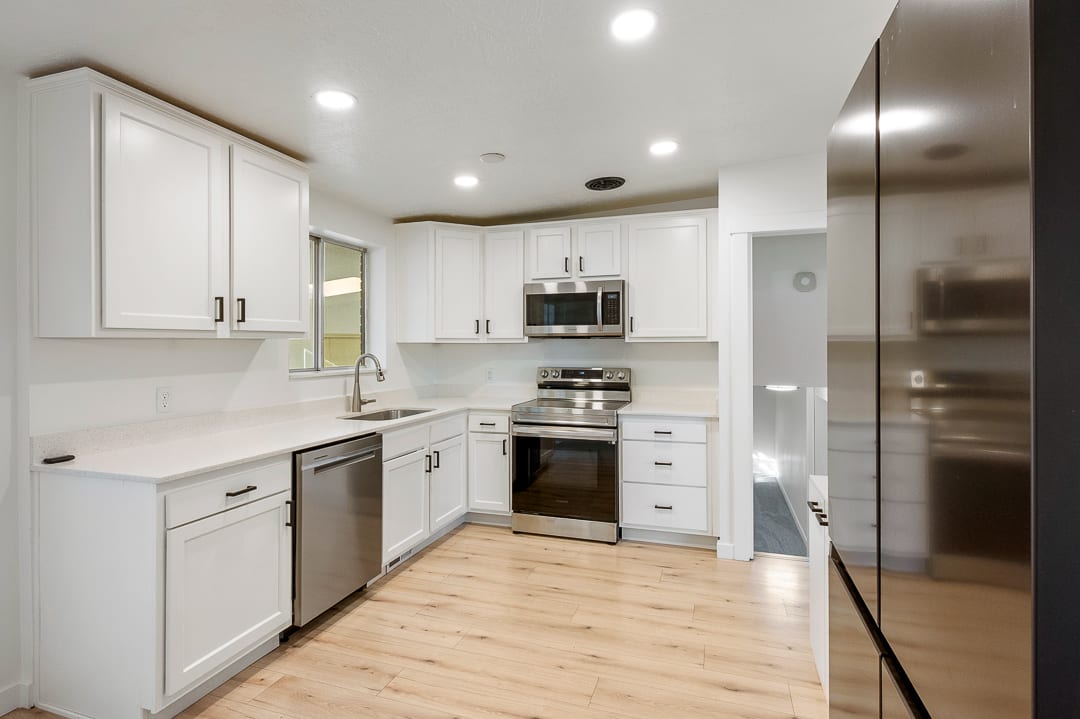 Contemporary kitchen featuring white cabinetry with matte black hardware, stainless steel appliances, light-toned countertops, and wood-finish flooring