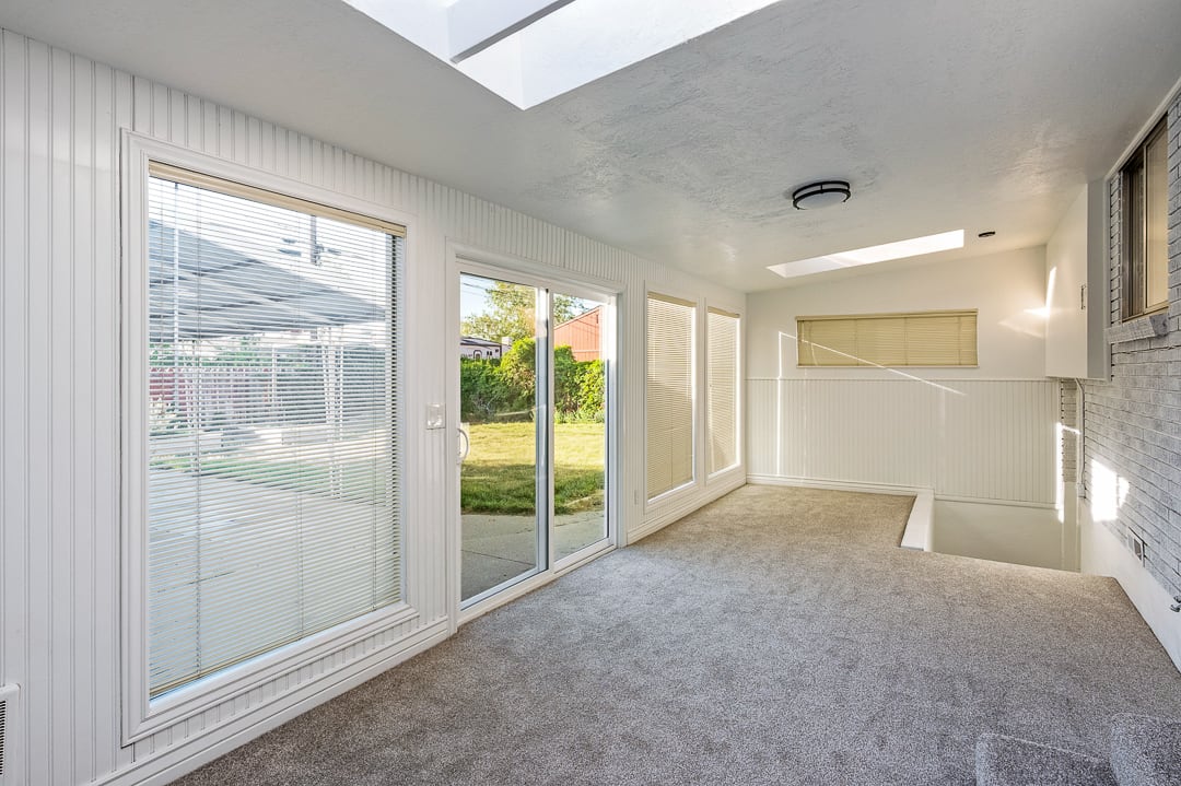 Carpeted interior space featuring multiple skylights, sliding glass door access to the exterior, and white paneled walls