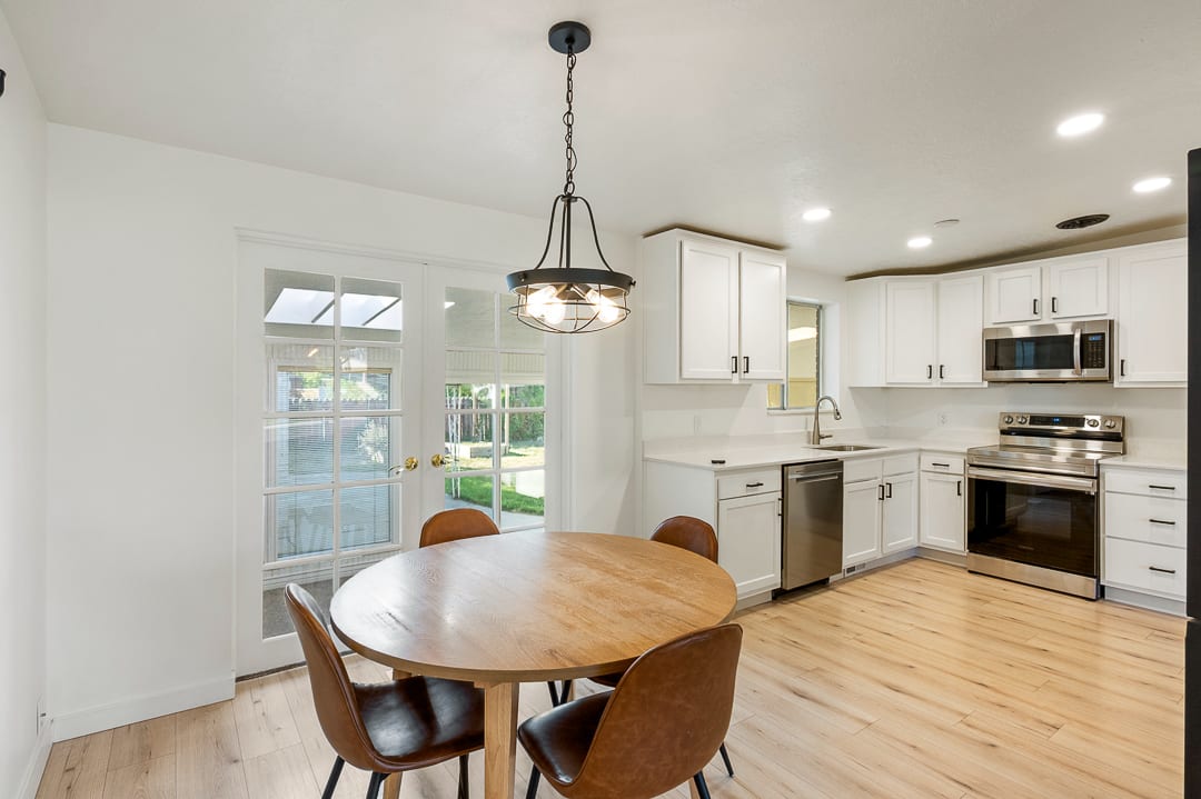 Contemporary kitchen featuring white cabinetry, stainless steel appliances, recessed lighting, wood-finish flooring, and double French doors opening to sunroom
