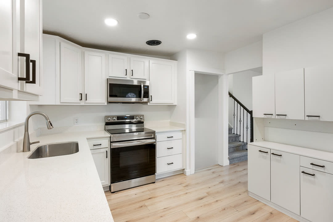 Modern kitchen featuring white cabinetry, light-toned wood-finish flooring, stainless steel appliances, and white countertops