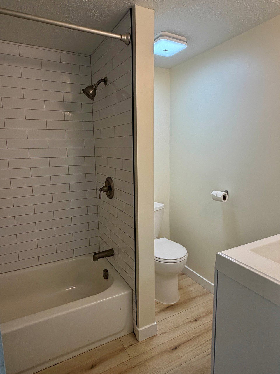 Bathroom featuring a white bathtub, subway tile surround, wood-finish flooring, and a white vanity with an integrated sink