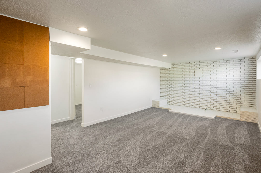 Spacious room featuring new gray carpeting, white painted brick wall, recessed lighting.