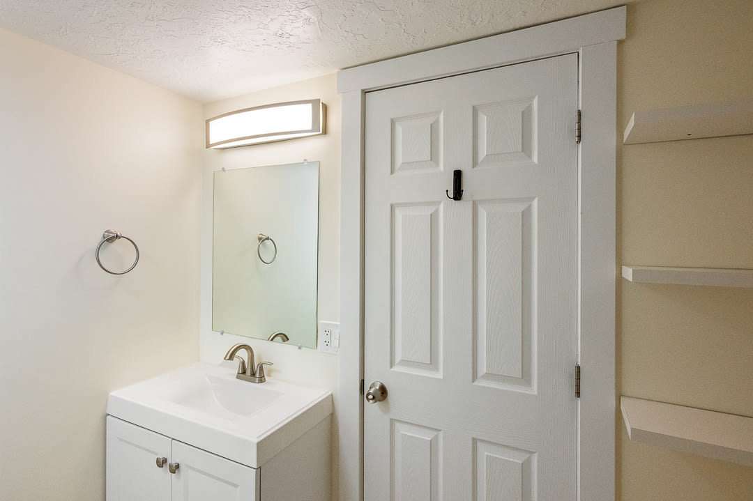 Bathroom vanity featuring a white cabinet, integrated sink, brushed nickel faucet, and rectangular mirror with an overhead light fixture