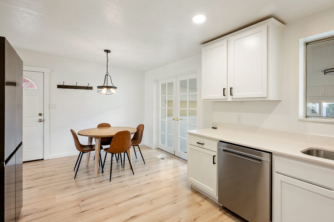 Eat-in kitchen featuring light wood-finish flooring, white cabinetry with dark hardware, a stainless steel dishwasher, and a light-toned countertop