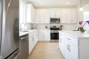 Modern kitchen featuring white cabinetry, stainless steel appliances, light-toned wood-finish flooring, a kitchen island, and recessed lighting