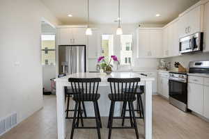 Modern kitchen featuring a large central island, light wood-finish flooring, white cabinetry, stainless steel appliances, and recessed lighting