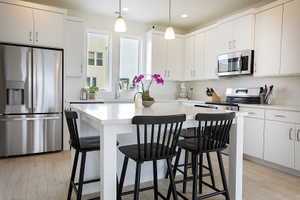 Kitchen featuring a central island with countertop seating, white cabinetry, stainless steel appliances, and wood-finish flooring