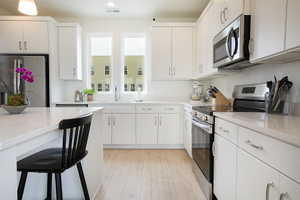 Bright kitchen featuring white cabinetry, light-toned countertops, stainless steel appliances, and wood-finish flooring