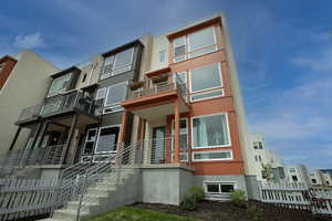 Multi-level contemporary townhome with a distinctive orange facade, multiple balconies with metal railings, large windows, and a white picket fence