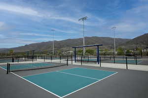Multiple pickleball courts featuring a hard court surface, perimeter fencing, overhead lighting, and shaded seating areas