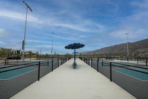 Outdoor recreation area featuring multiple courts with green and gray surfacing, black chain-link fencing, and overhead lighting