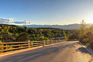 Paved road descending through a treed hillside community, with distant mountains and a valley visible